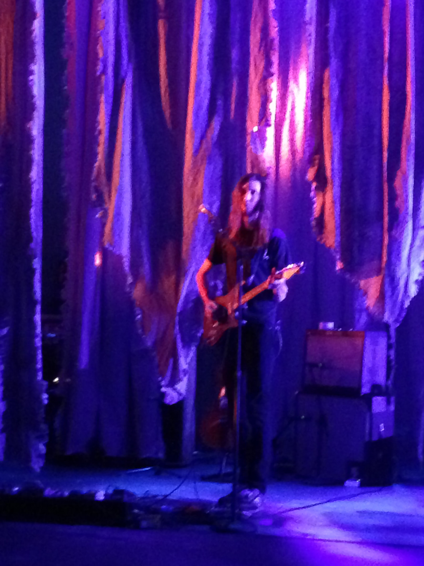 Medea — solo guitarist in a spotlight against draped curtains