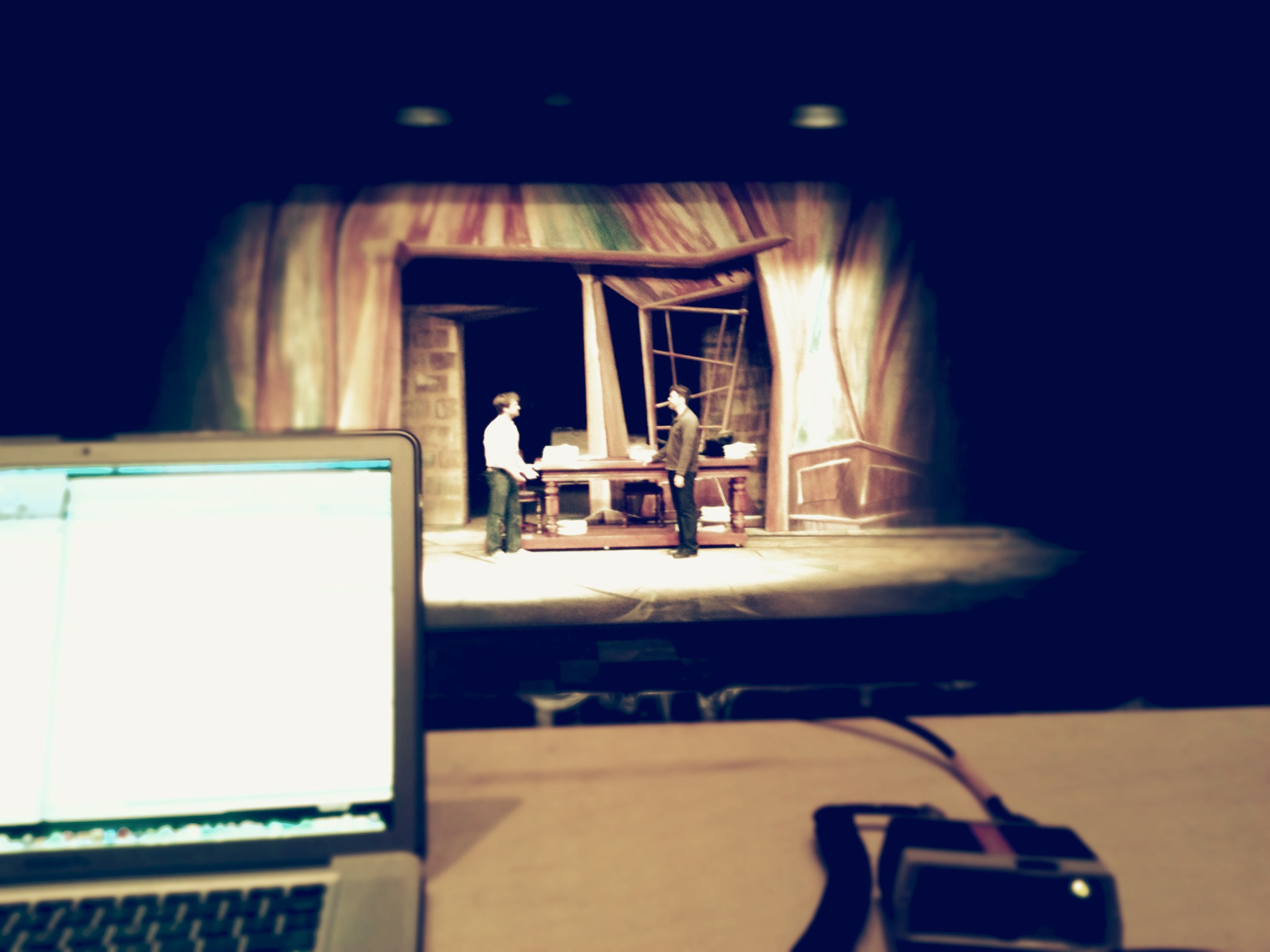 The Understudy — view from the tech table during rehearsal, laptop running cues in front of the painted set