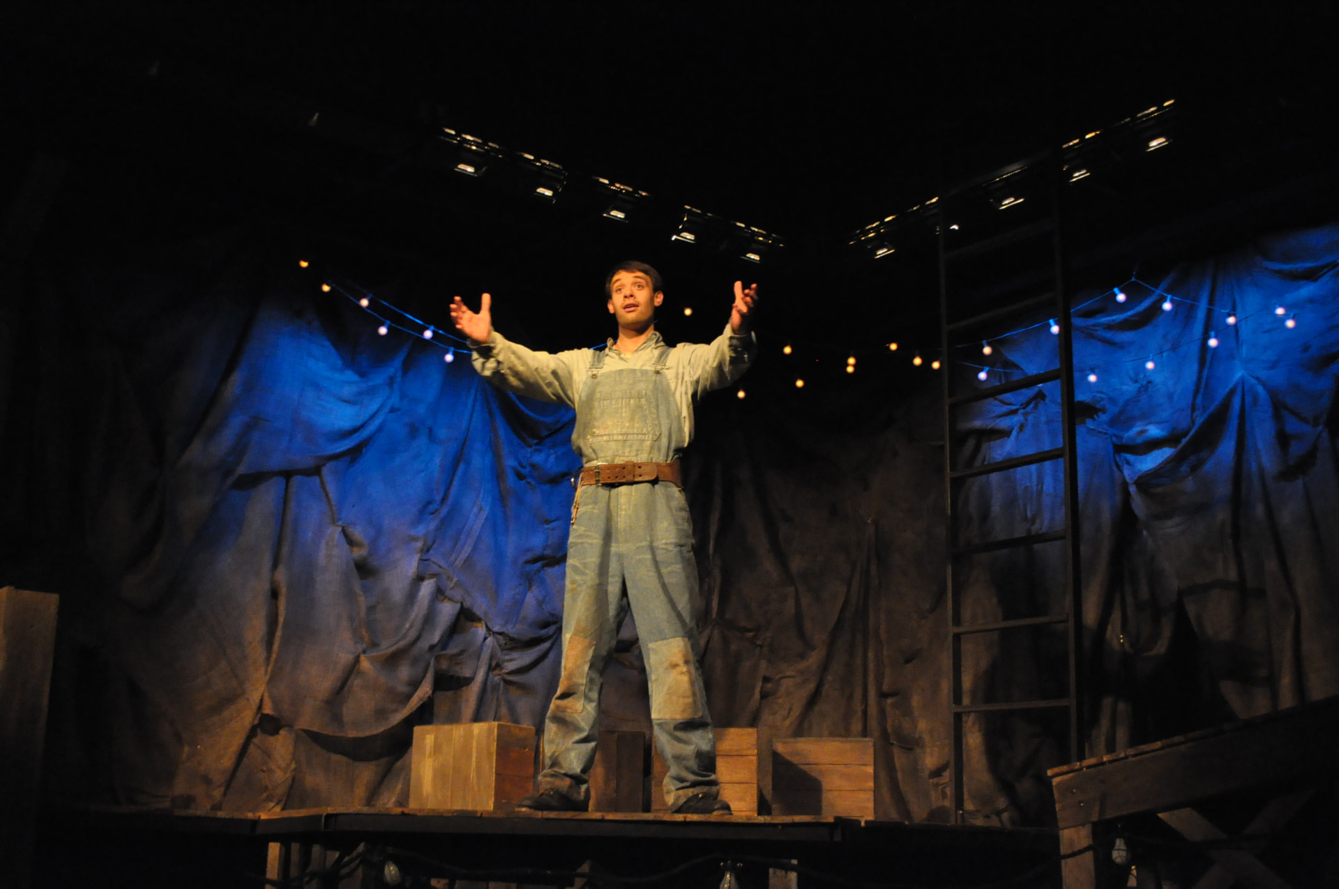 Floyd Collins — Floyd singing with arms outstretched beneath strings of practical lights
